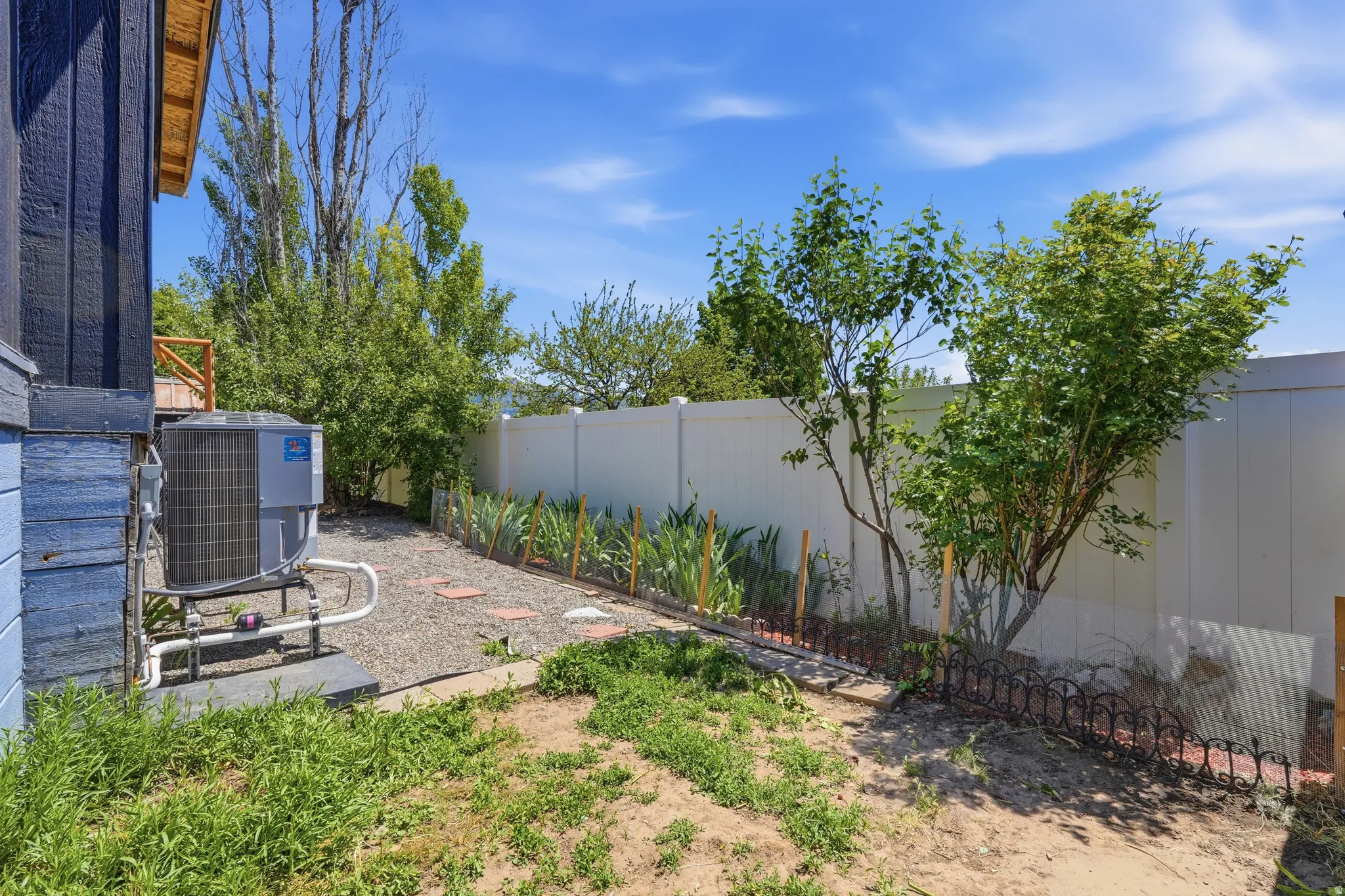Side yard featuring a gravel pathway with stepping stones, mature trees, and a privacy fence
