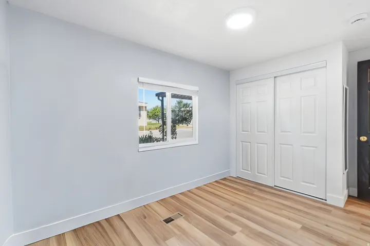 Room featuring wood-finish flooring, a window with a roller shade, and white paneled sliding closet doors