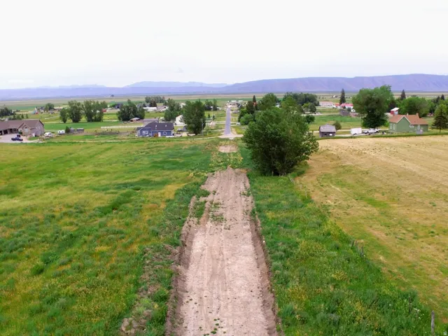 Expansive open fields with a developing dirt road extending towards a distant community