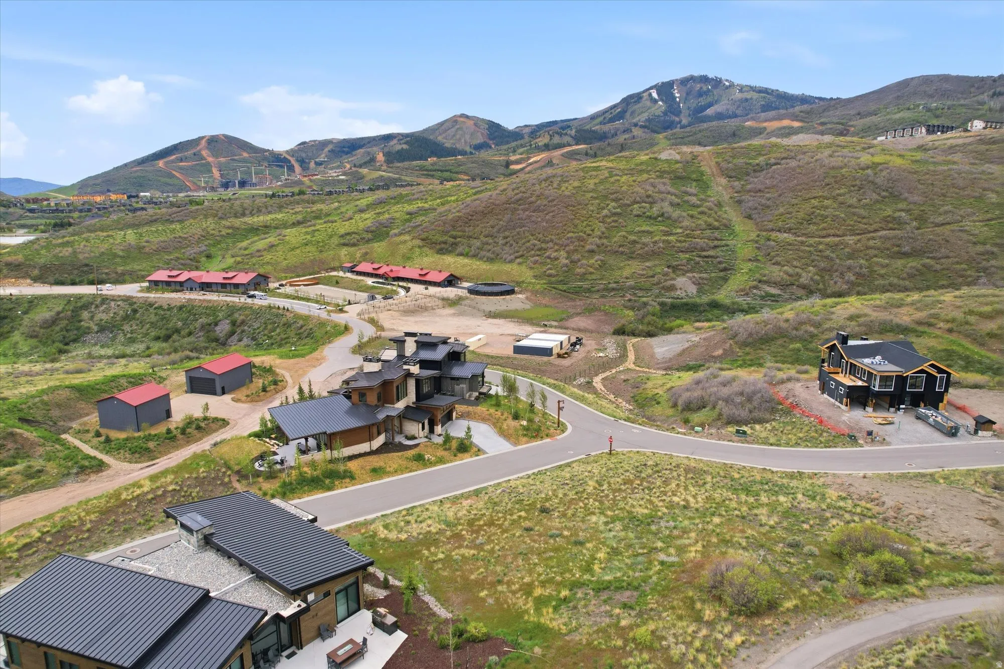 Expansive mountainous terrain featuring a winding paved road, several modern properties with dark metal roofing, and multiple structures under construction