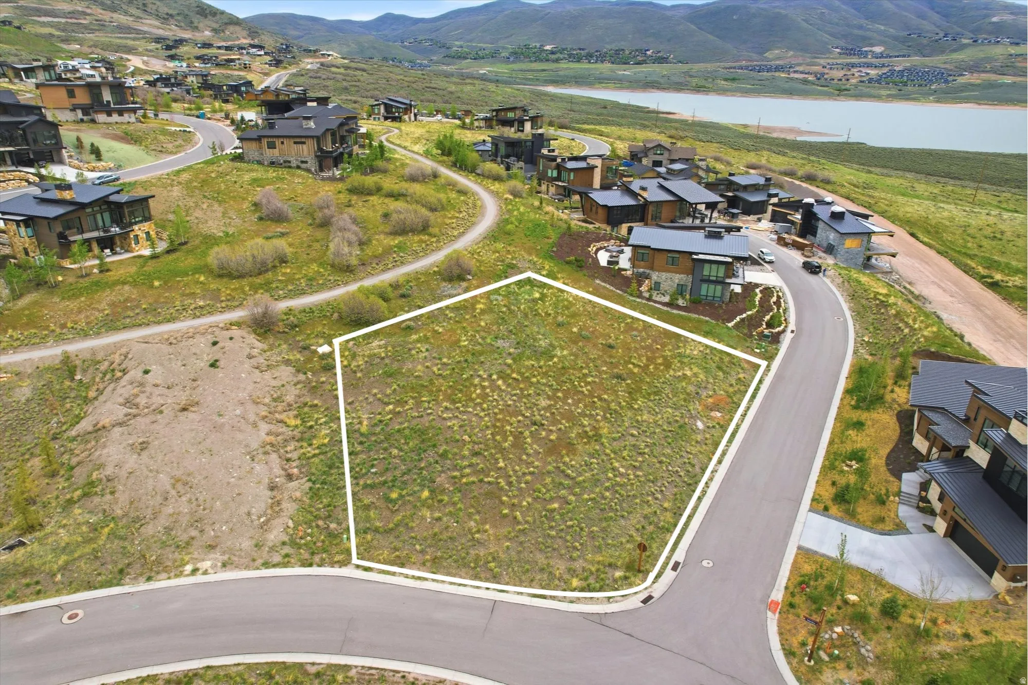 Spacious undeveloped lot featuring a paved road frontage, surrounding residential properties, and a distant body of water