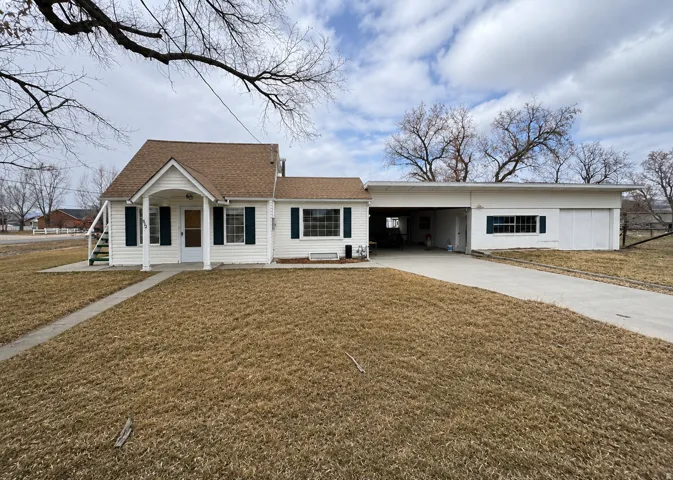 Traditional-style home featuring white siding, dark shutters, a covered entry porch, a multi-car driveway, and an attached carport