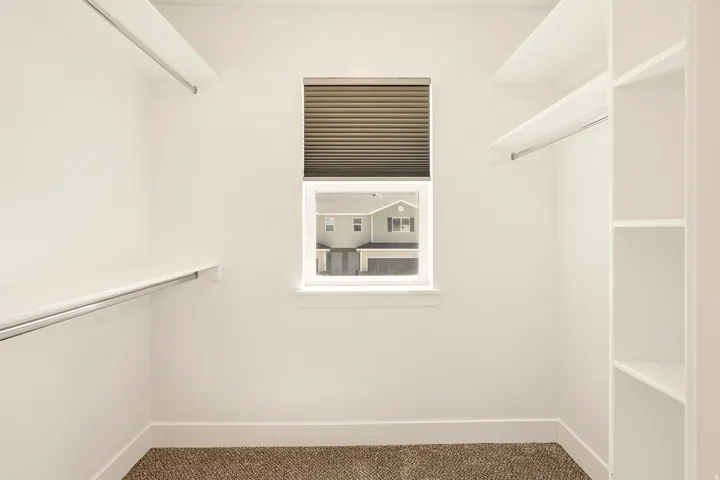 Walk-in closet with built-in shelving, hanging rods, and a window with blinds