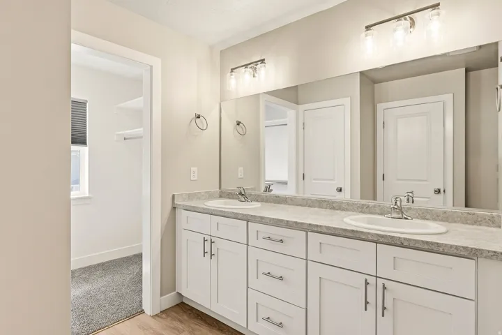 Bathroom vanity featuring dual sinks with individual faucets, a full-width mirror, and a three-light fixture