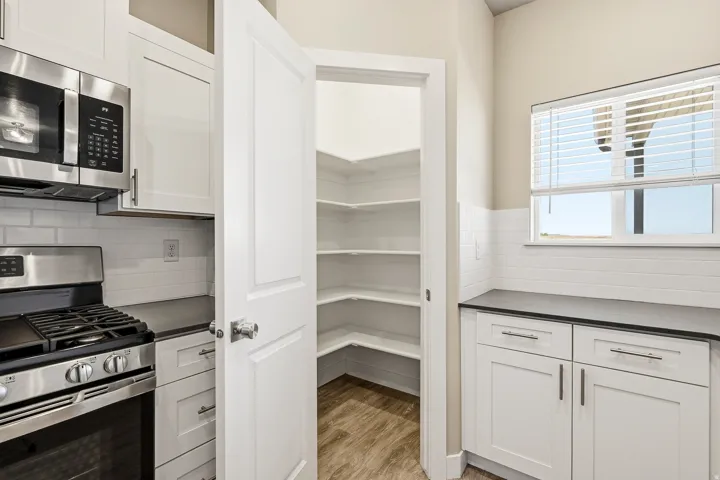 Kitchen featuring white cabinetry, dark countertops, a stainless steel range with overhead microwave, white subway tile backsplash, and a walk-in pantry with wood-finish flooring