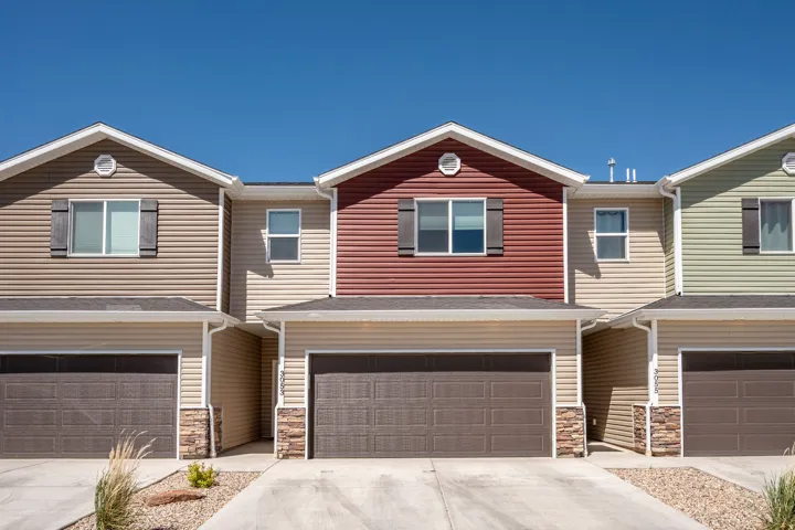 Townhome exterior featuring horizontal siding in varied earth tones, attached garage, stone veneer accents, and concrete driveways
