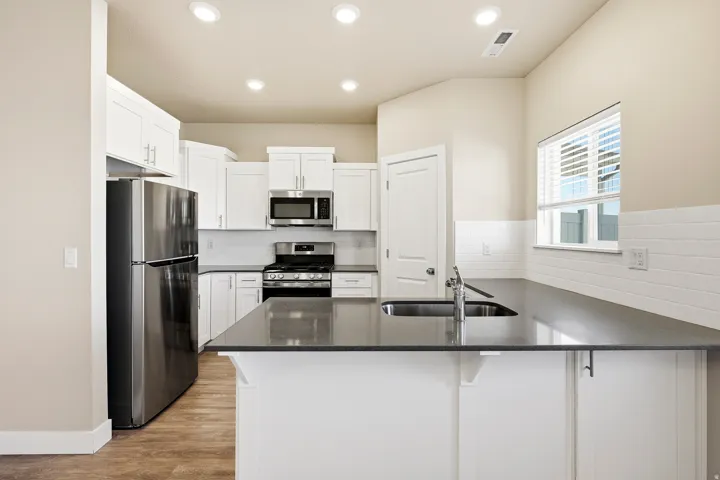 Kitchen featuring white cabinetry with silver hardware, dark countertops, stainless steel appliances, and a subway tile backsplash
