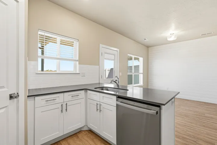 Contemporary kitchen featuring white cabinetry, dark countertops, a stainless steel dishwasher, an undermount sink with a gooseneck faucet, and subway tile backsplash