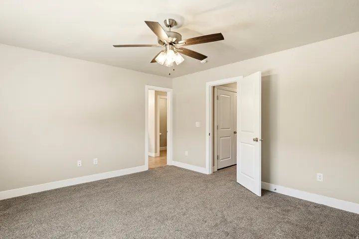 Carpeted room featuring a ceiling fan with integrated lighting, neutral wall paint, white trim, and a paneled interior door
