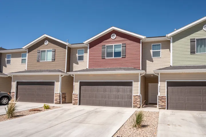 Multi-level townhome featuring a two-car garage, stone facade accents, and horizontal siding