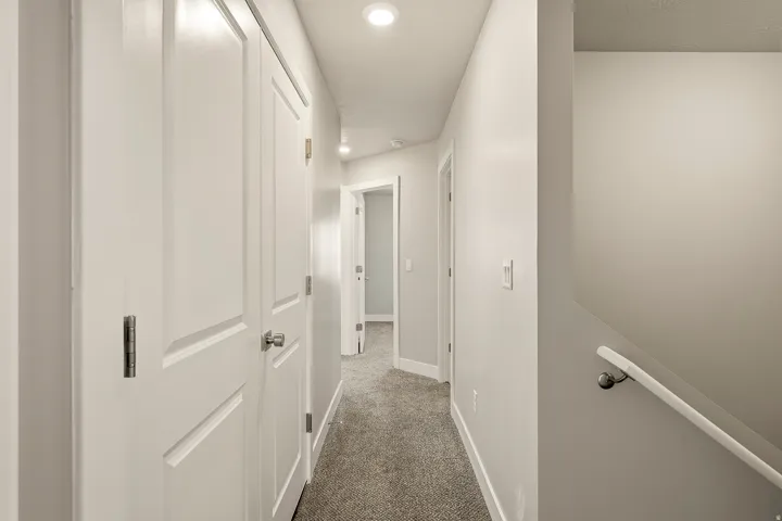 Hallway featuring recessed lighting, paneled doors, light grey wall paint, grey carpet flooring, and a white handrail