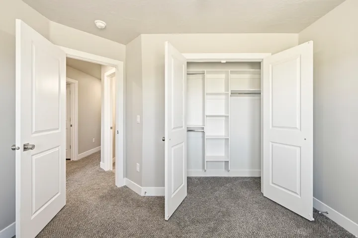 Bedroom featuring neutral carpet flooring, light gray wall paint, and a built-in closet system with shelving and hanging rods