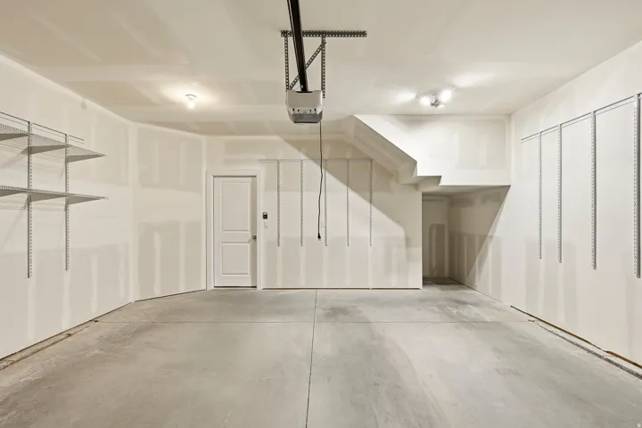 Spacious garage with concrete flooring, overhead lighting, and built-in shelving tracks for customizable storage
