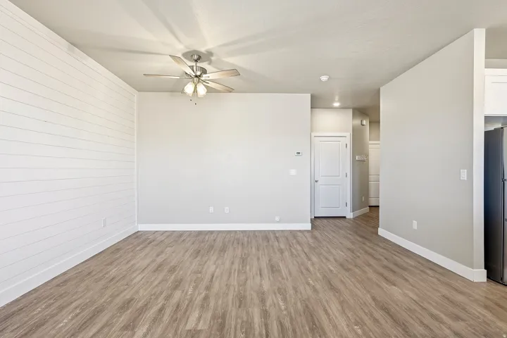 Open concept living space featuring wood-finish flooring, a shiplap accent wall, and a ceiling fan with integrated lighting