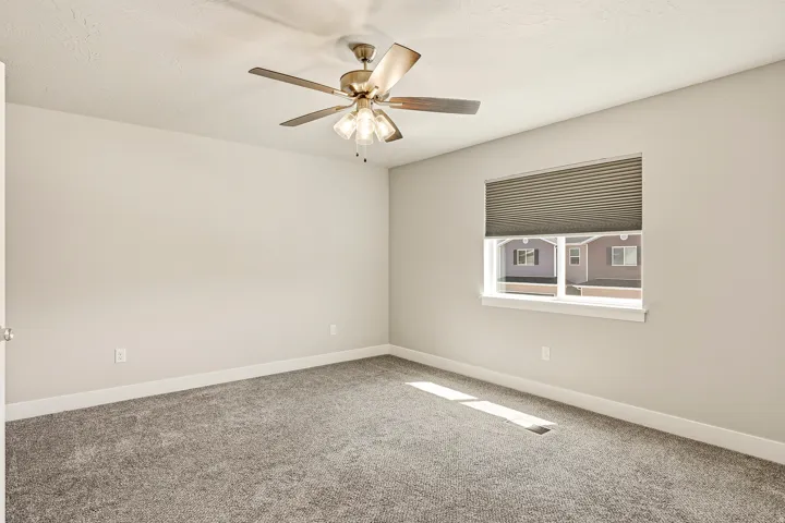 Bright interior room featuring a window with blinds, a ceiling fan with integrated lighting, and neutral-toned carpeting