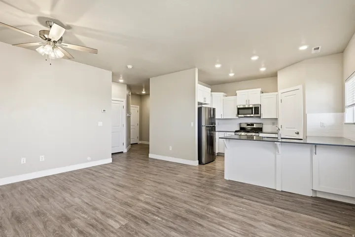 Open-concept living space featuring wood-finish flooring, a ceiling fan, recessed lighting, and a kitchen with white cabinetry, stainless steel appliances, and a breakfast bar