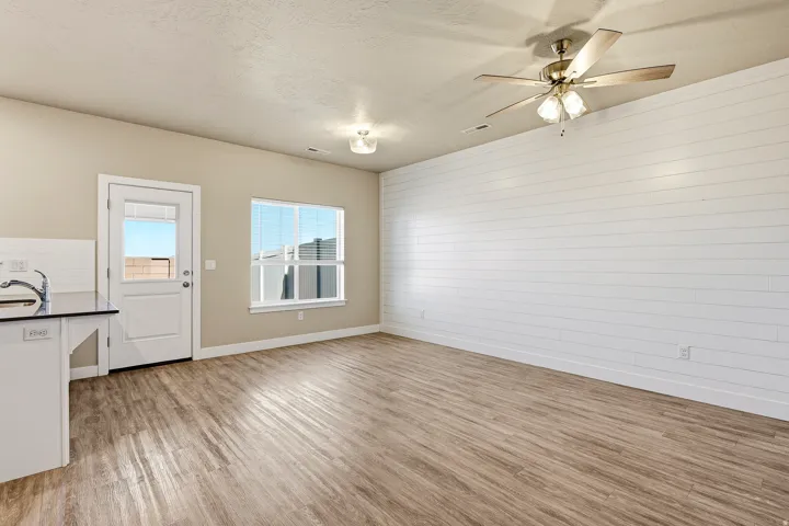 Open concept living area featuring wood-finish flooring, a shiplap accent wall, and a ceiling fan with integrated lighting