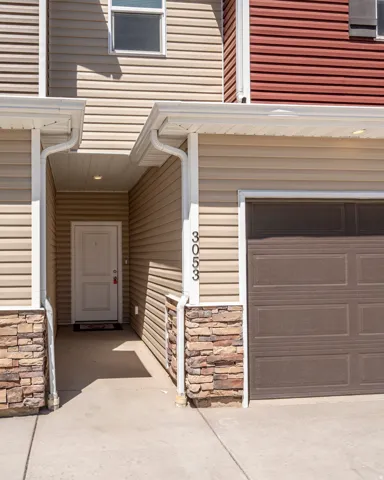 Exterior featuring multi-toned siding, stone veneer accents, an attached garage, a covered entry, and a white front door