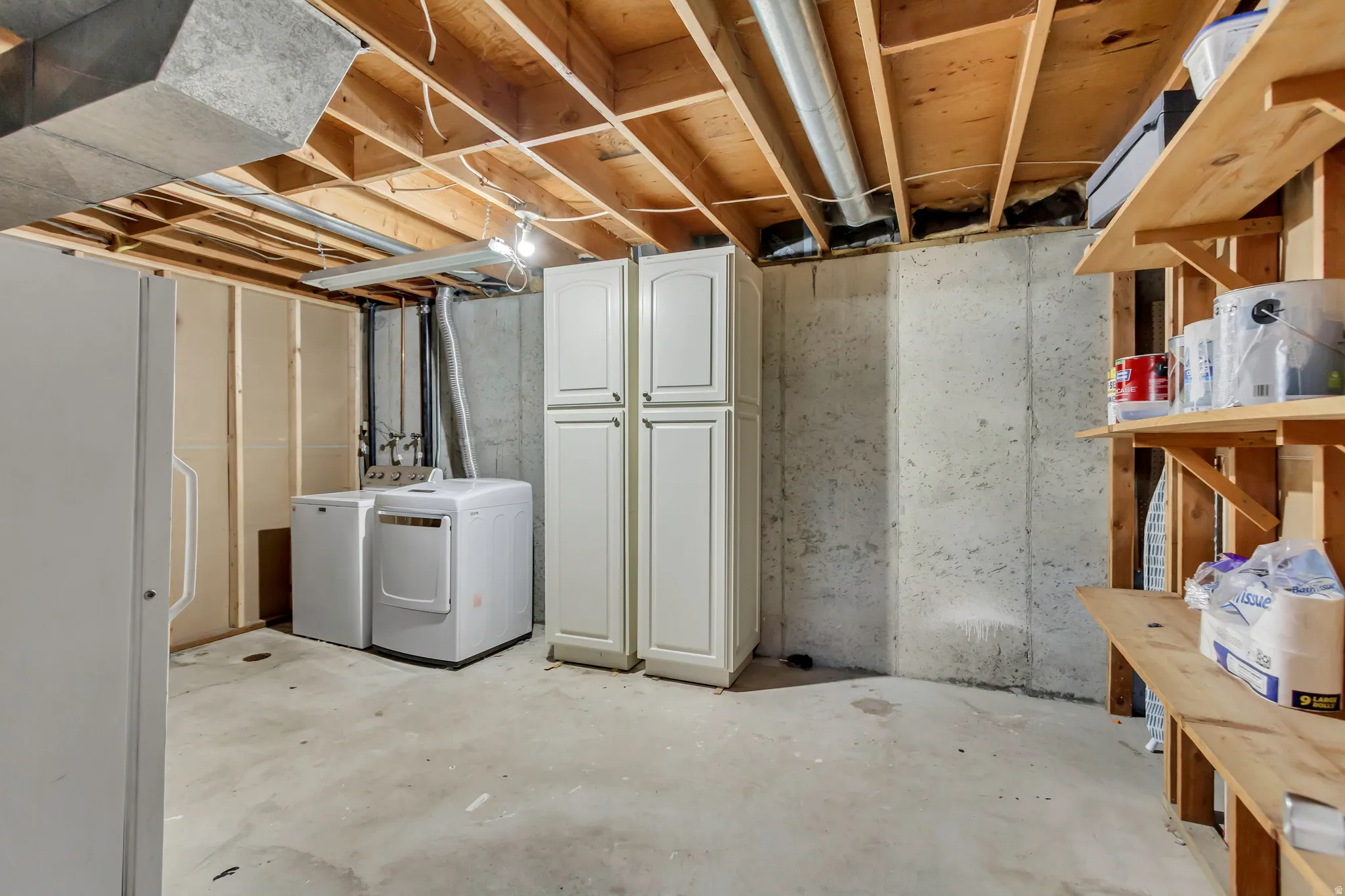 Unfinished basement space featuring exposed wood joists, concrete flooring, and built-in wood shelving for storage