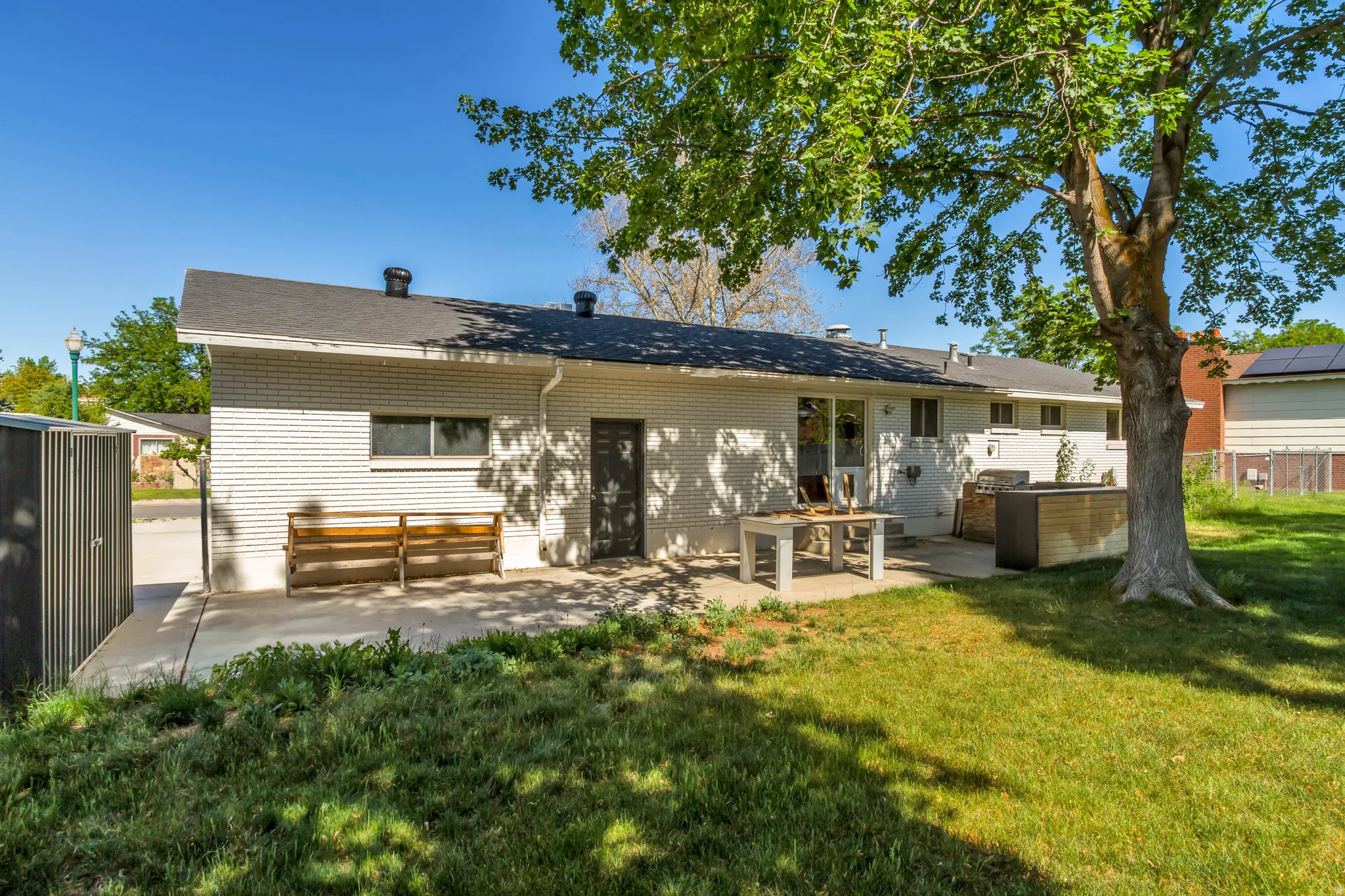 Rear exterior featuring a concrete patio, white brick facade, and a mature shade tree