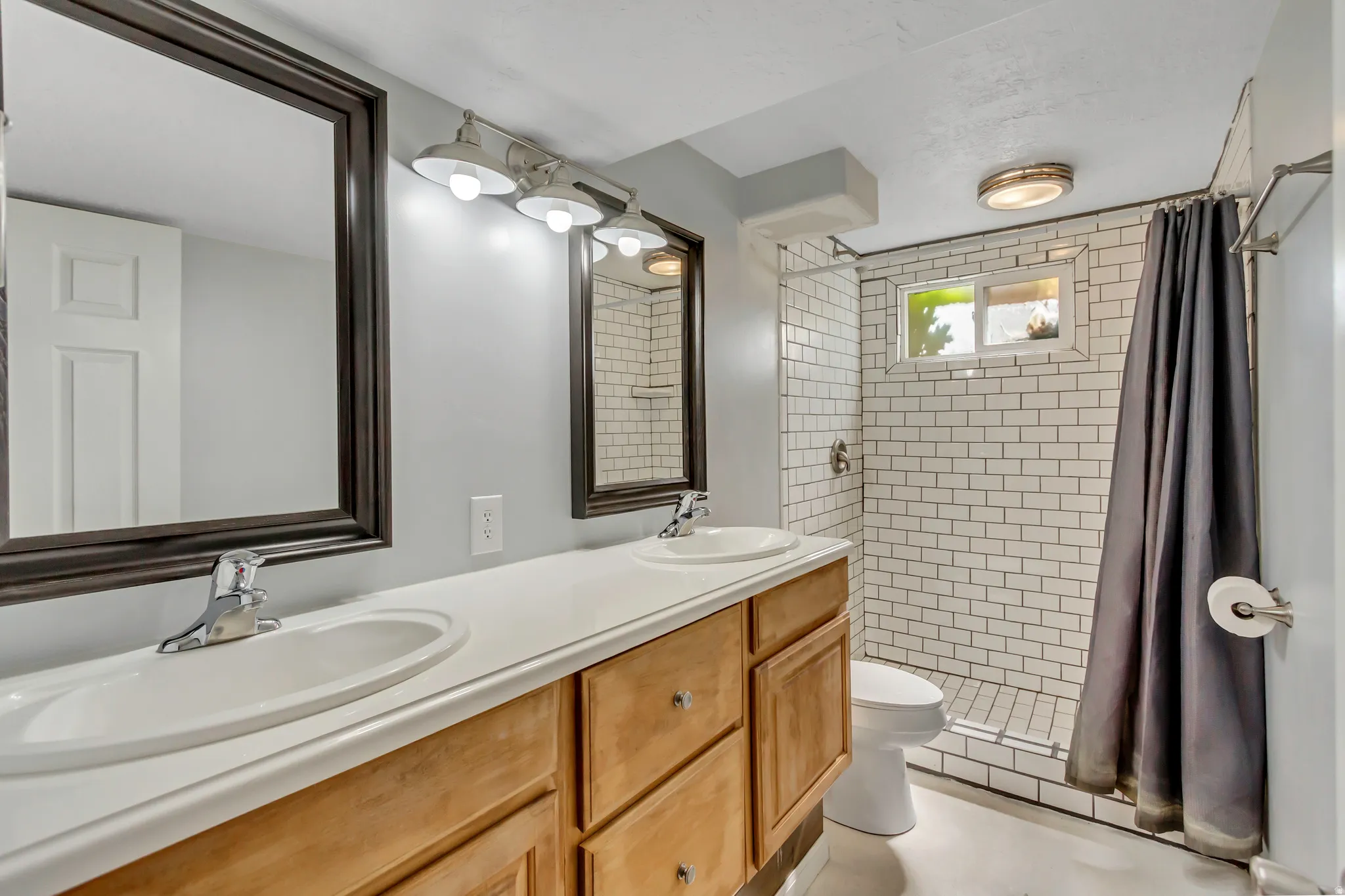 Bathroom featuring a dual vanity with wood cabinetry and framed mirrors, a shower with white subway tile surround, and a compact window
