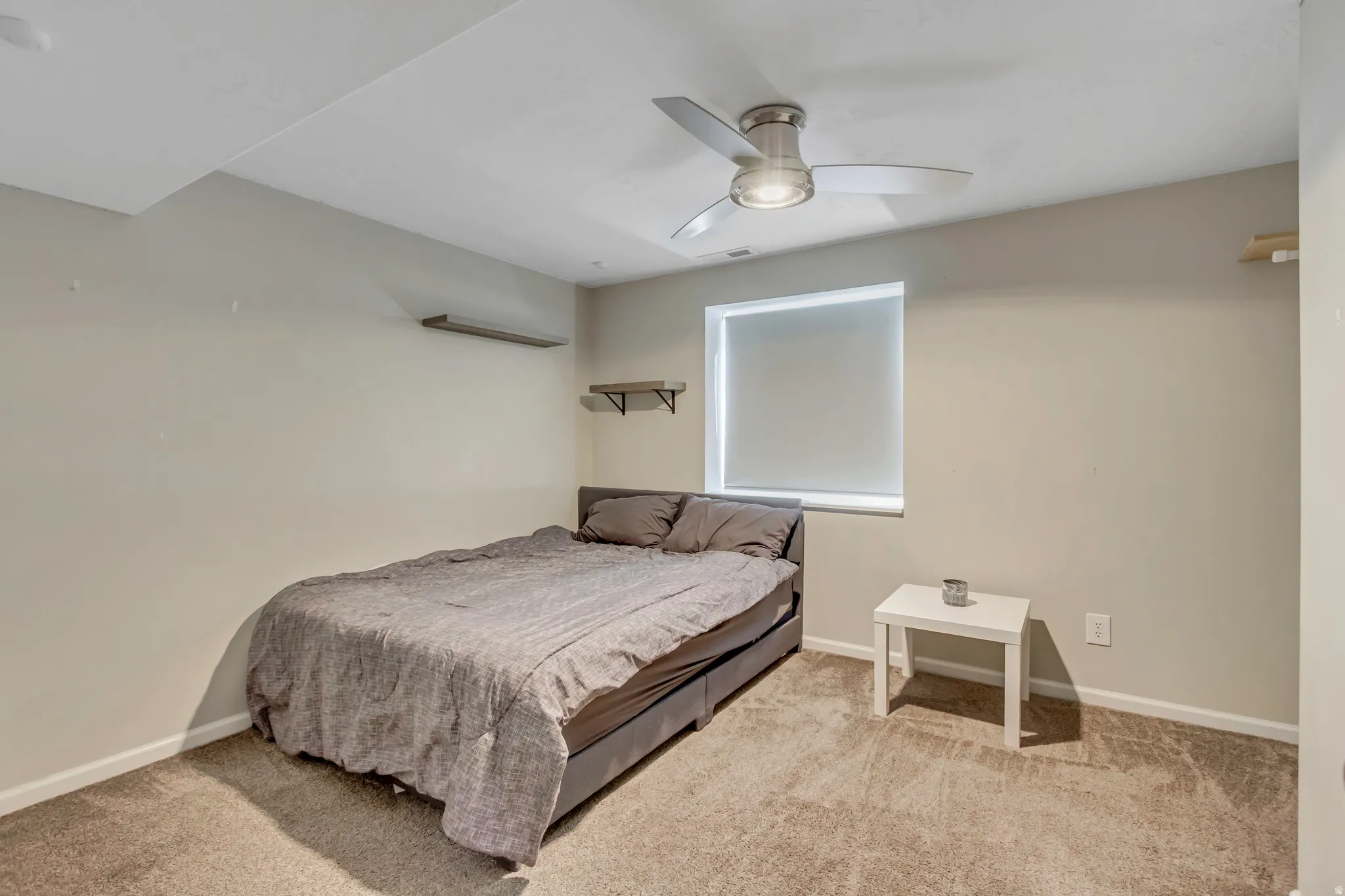 Room featuring neutral wall tones, textured carpeting, a single window with a roller shade, and a ceiling fan with integrated lighting