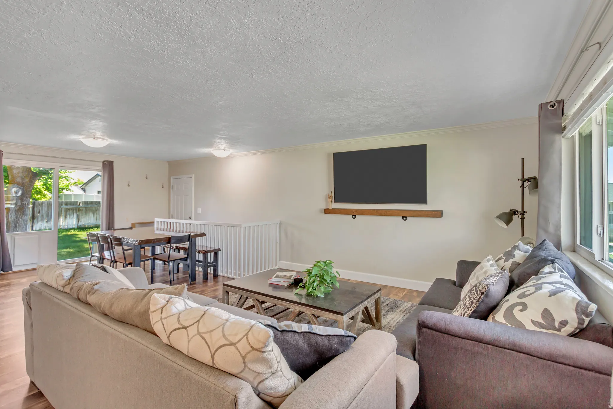 Open-concept living space with wood-finish flooring, a wall-mounted display shelf, and ample natural light from large windows and a glass sliding door