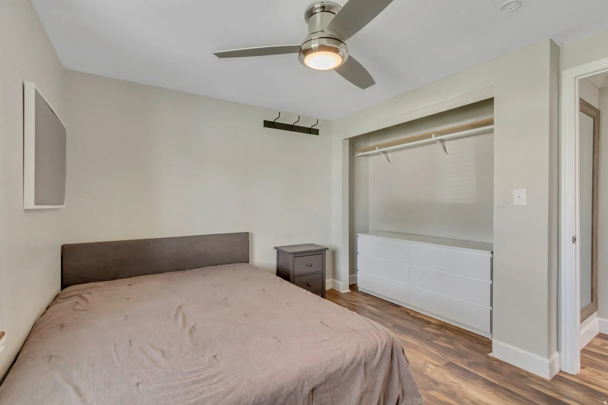Bedroom featuring wood-finish flooring, a contemporary ceiling fan with integrated lighting, and a built-in closet system with shelving and a white drawer unit