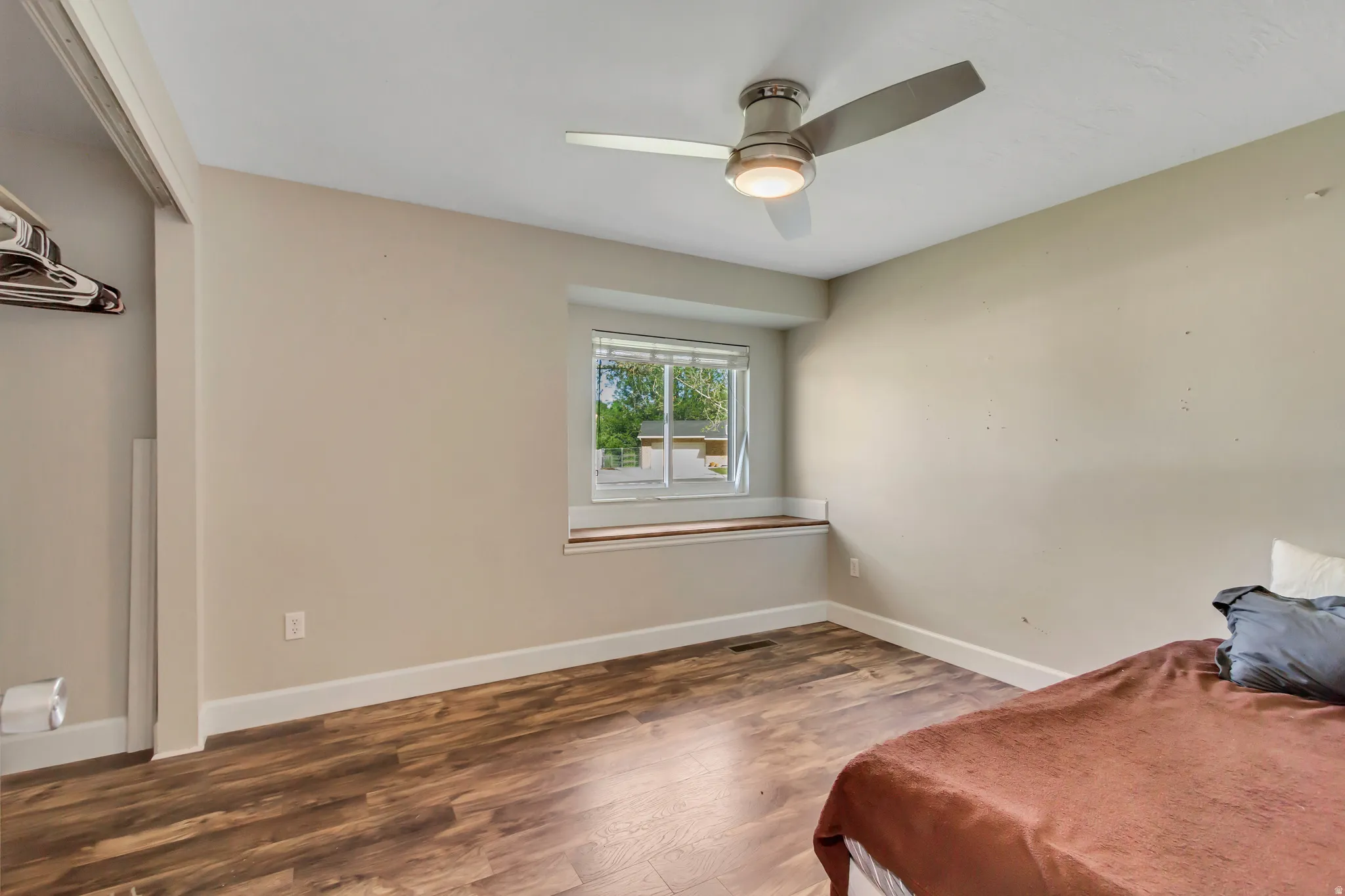 Room featuring wood-finish flooring, a window with a built-in sill, a ceiling fan with integrated lighting, and neutral wall tones