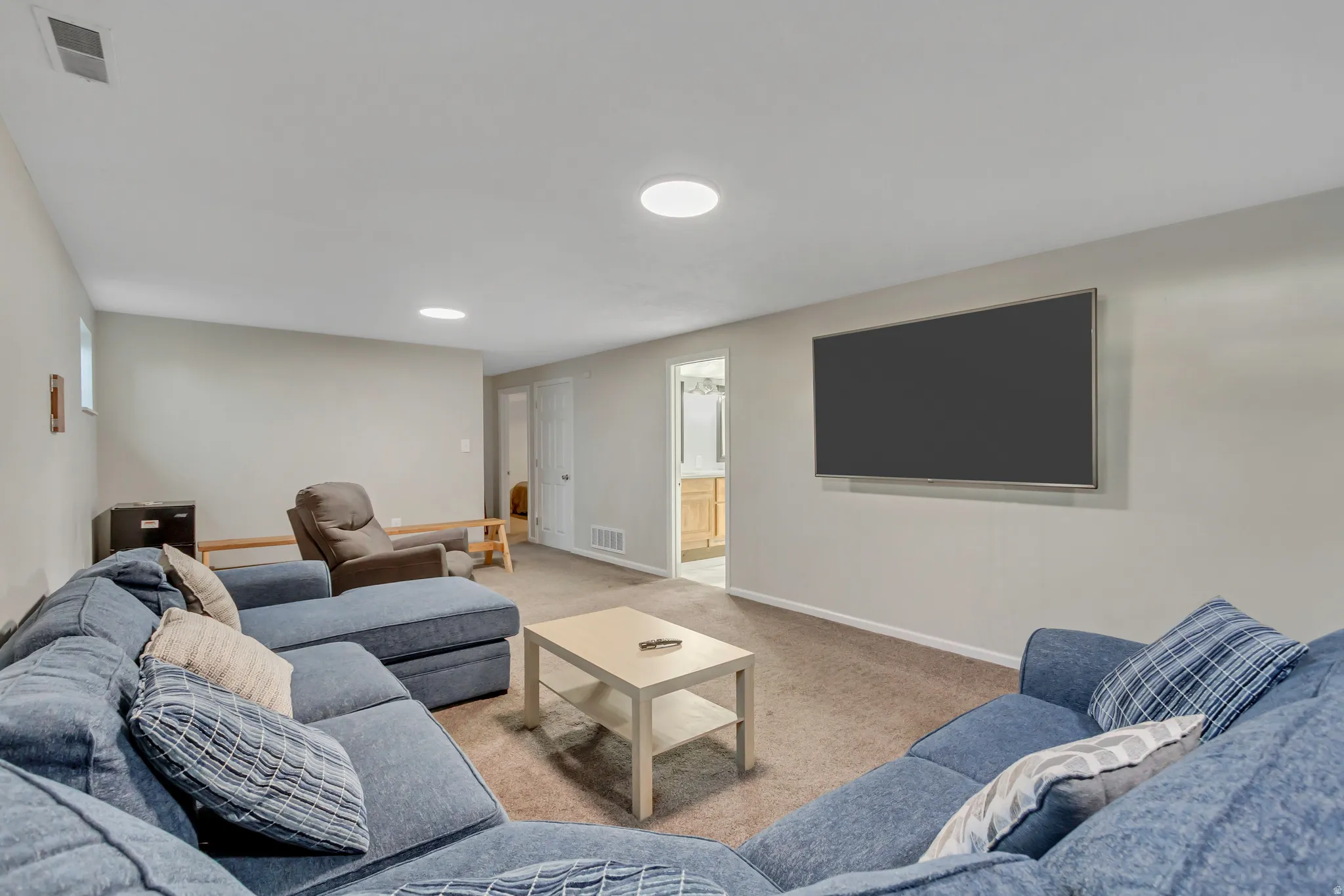 Spacious room featuring neutral wall paint, carpet flooring, a wall-mounted display, and recessed lighting