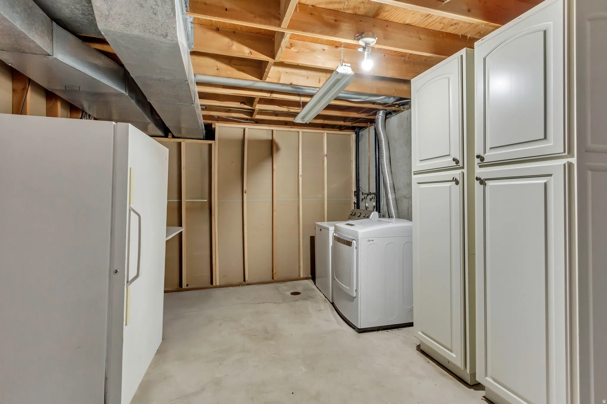Utility area featuring a washer and dryer, concrete flooring, exposed ceiling joists, and white built-in cabinetry