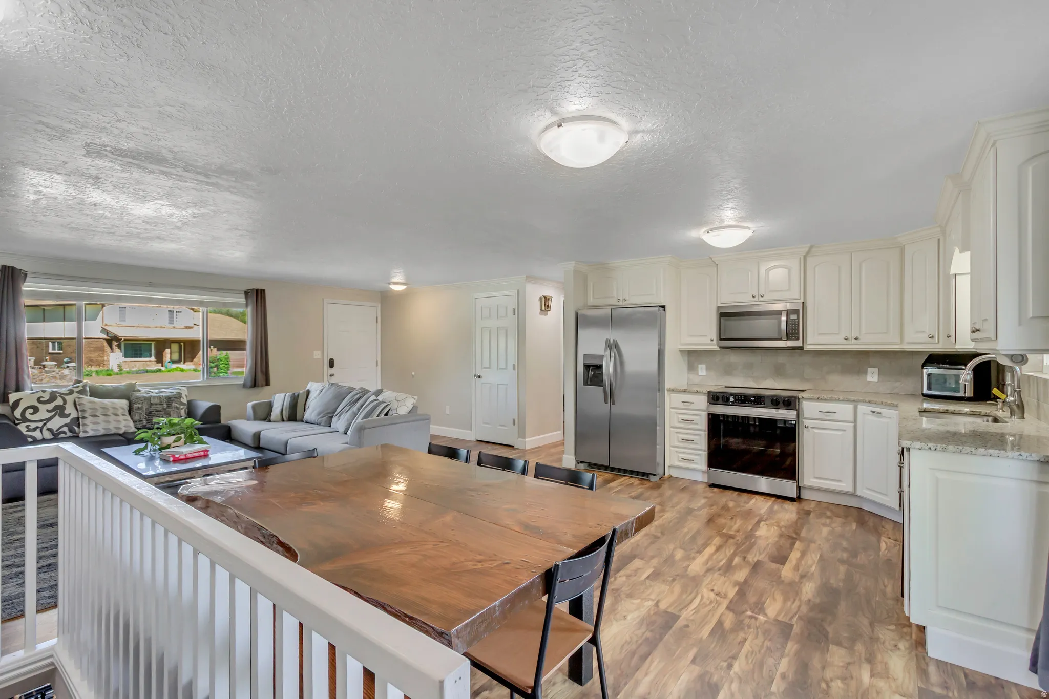 Open-concept living space featuring a kitchen with light-toned cabinetry, stainless steel appliances, and granite-style countertops