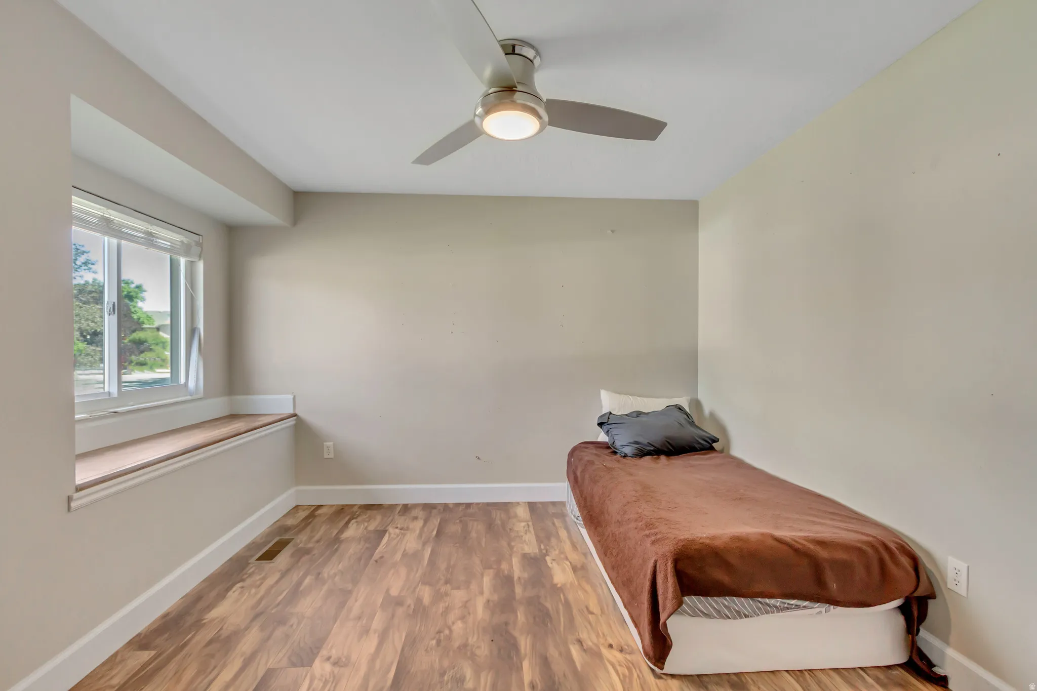 Recessed window with a built-in wood-finish window seat, wood-finish flooring, and a modern ceiling fan