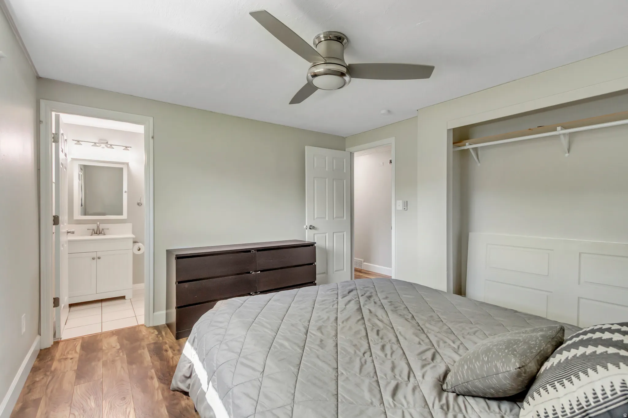 Bedroom featuring wood-finish flooring, a ceiling fan with integrated lighting, and an open closet with shelving and hanging rod