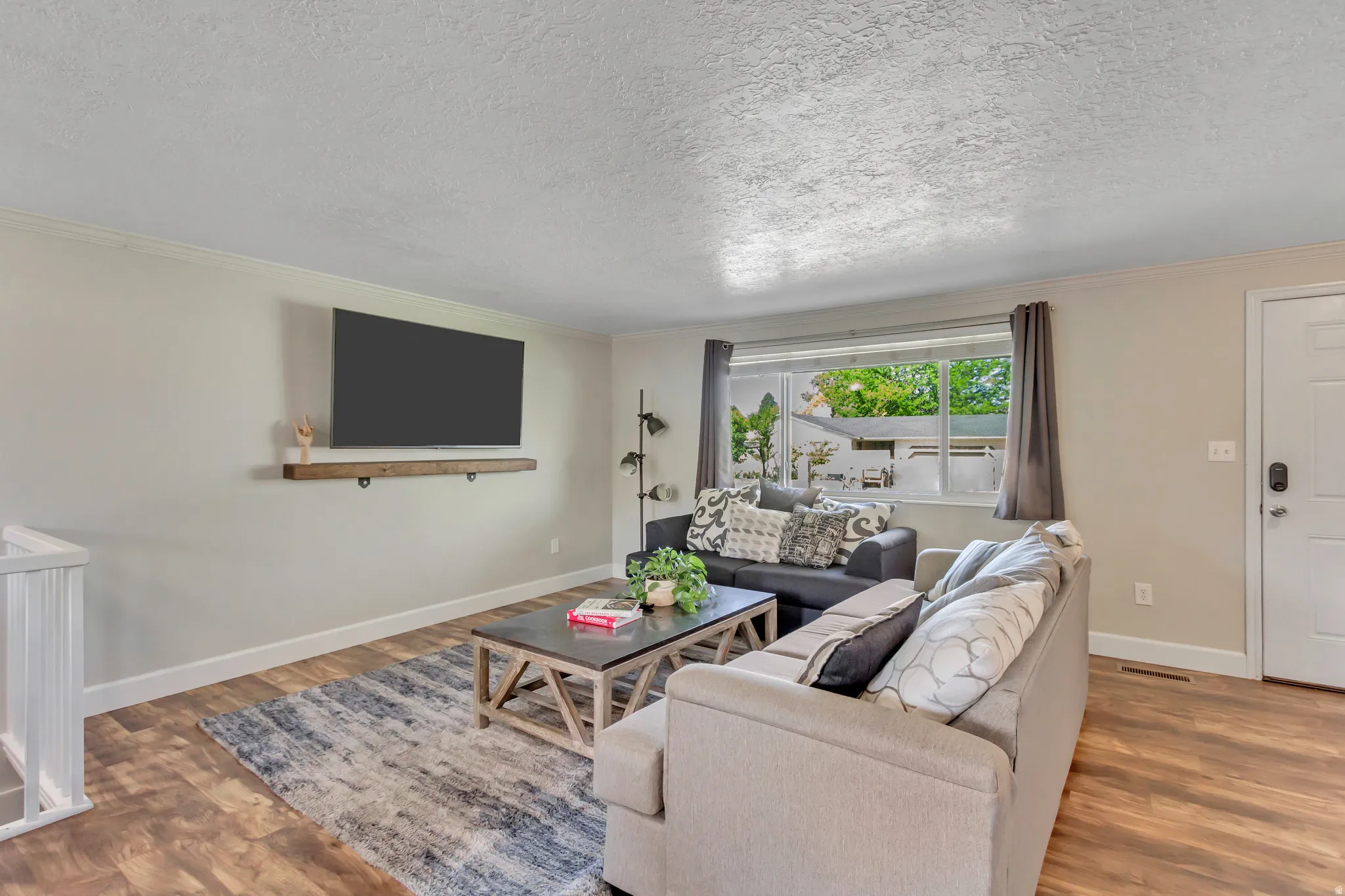 Spacious living area featuring wood-finish flooring, a contemporary floating shelf, and a large window