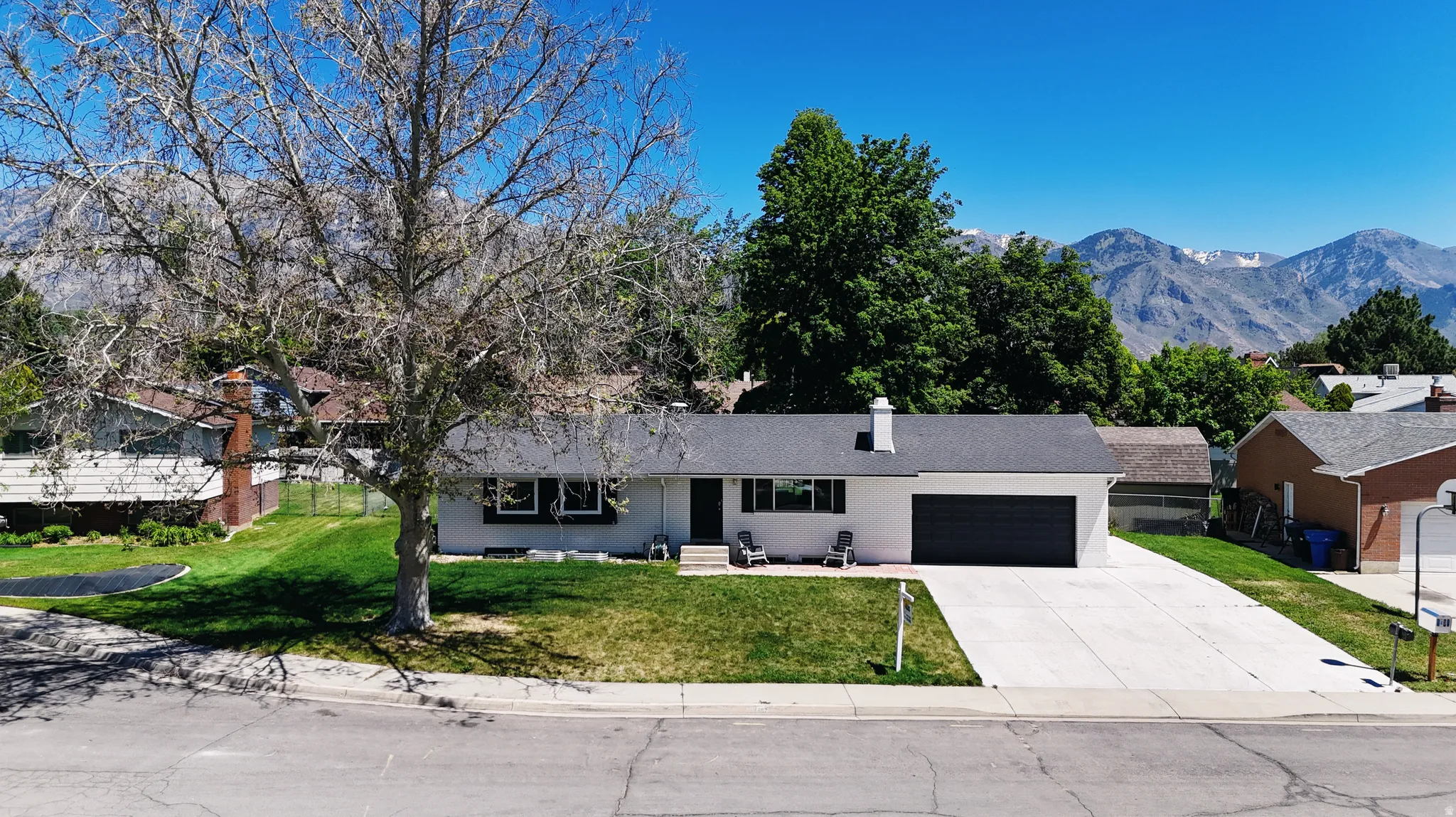Single-story residence featuring a white exterior, dark gray garage door, and a black shingle roof