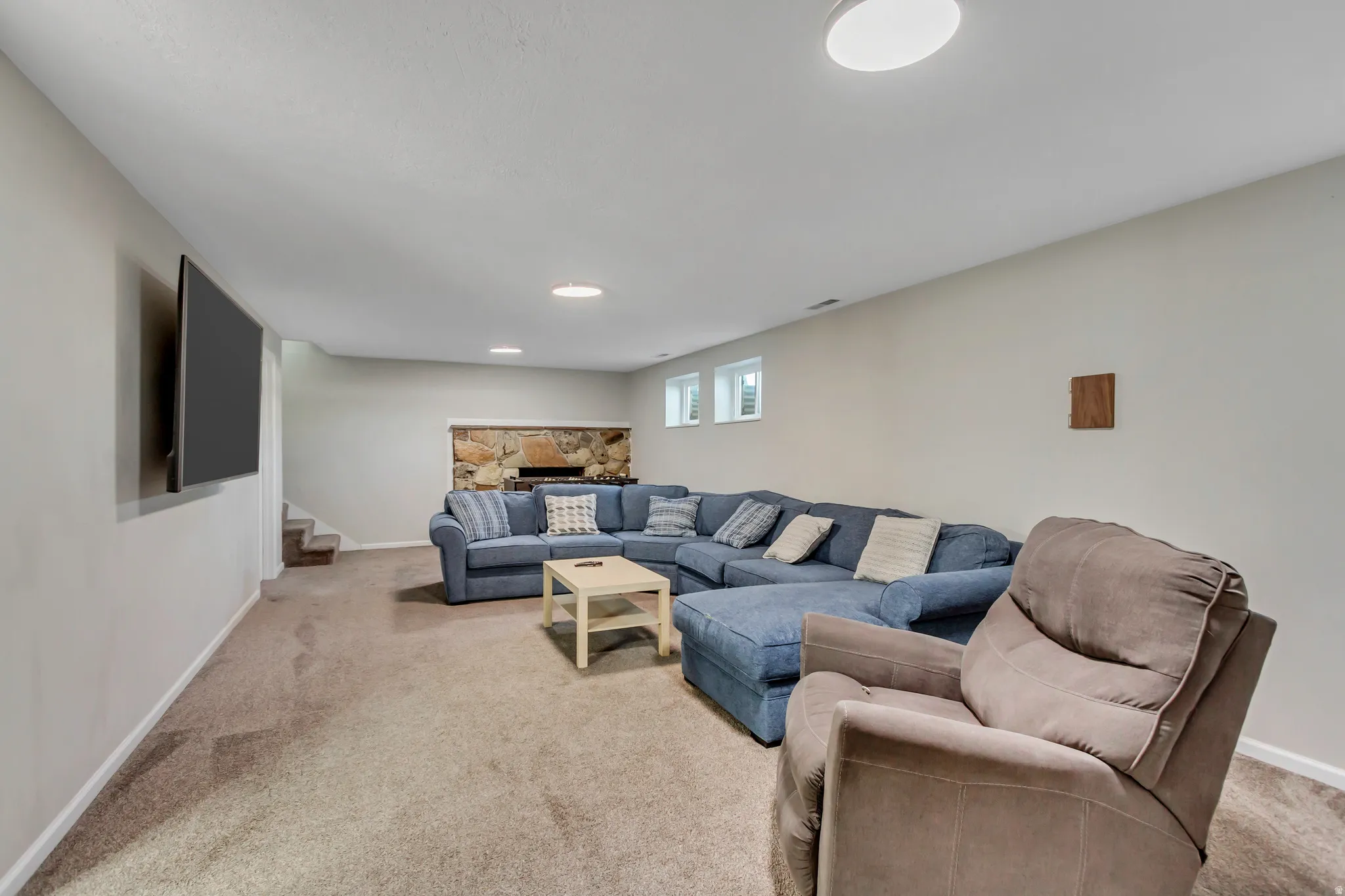 Spacious entertainment area featuring neutral-toned carpeting, recessed ceiling lighting, and a stone-clad fireplace