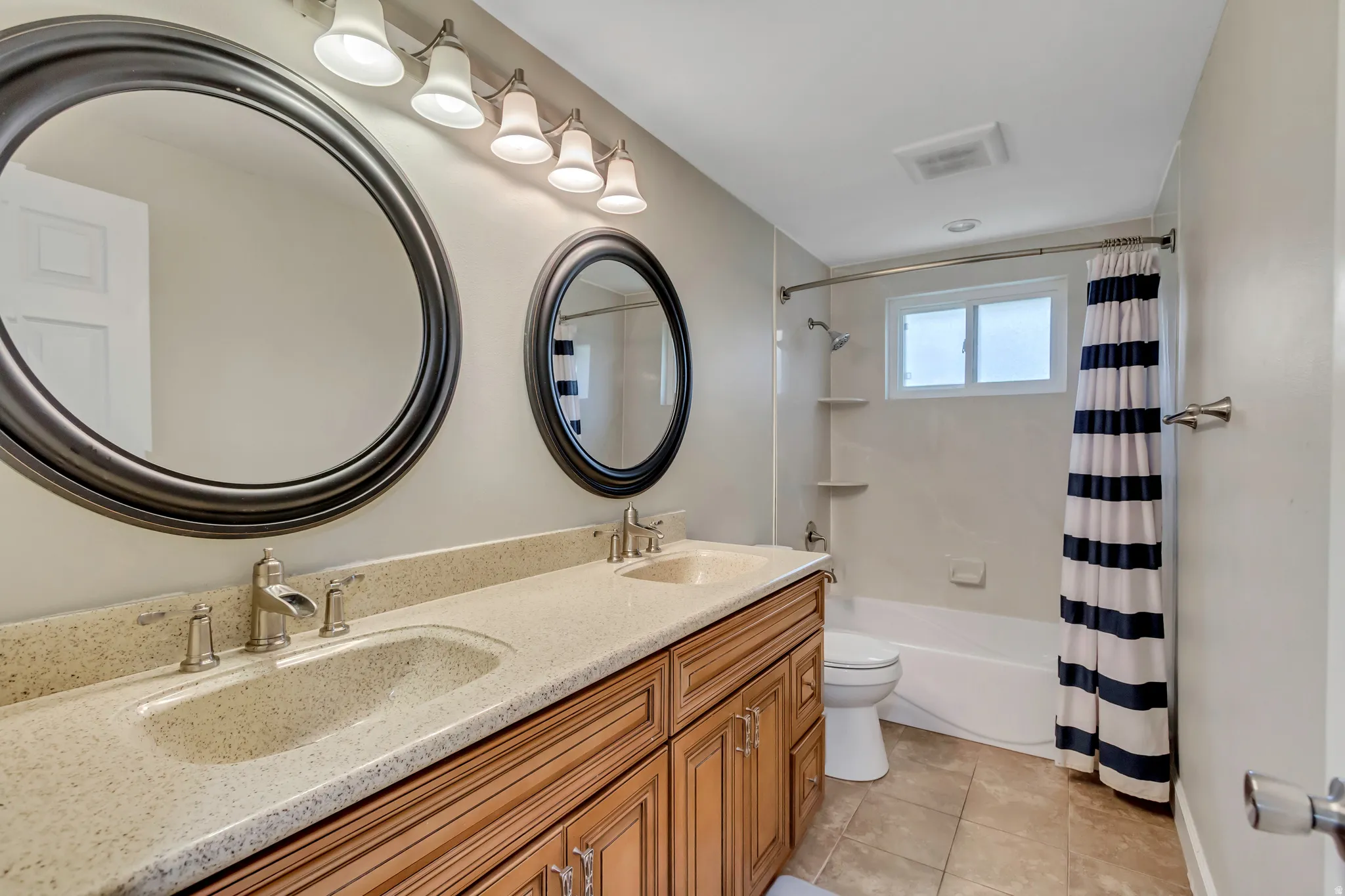Dual-sink vanity with light-toned countertop, wood-finish cabinetry, and circular mirrors