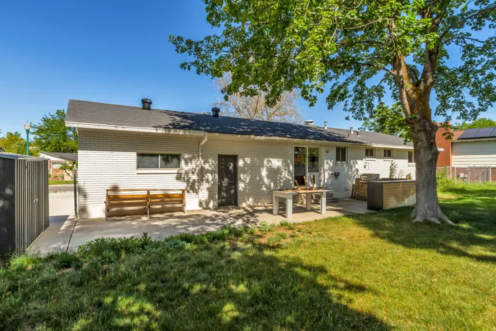 Rear exterior featuring a concrete patio, white brick facade, and a mature shade tree