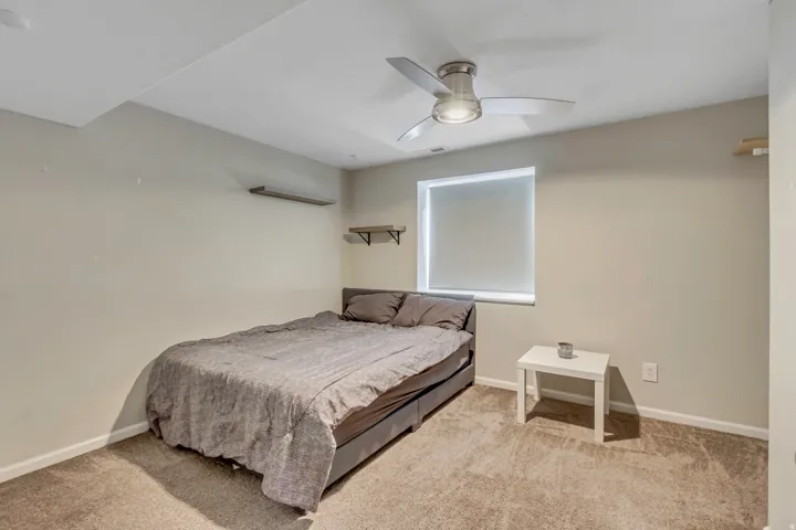 Room featuring neutral wall tones, textured carpeting, a single window with a roller shade, and a ceiling fan with integrated lighting