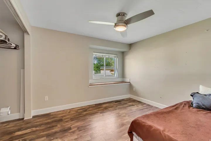 Room featuring wood-finish flooring, a window with a built-in sill, a ceiling fan with integrated lighting, and neutral wall tones