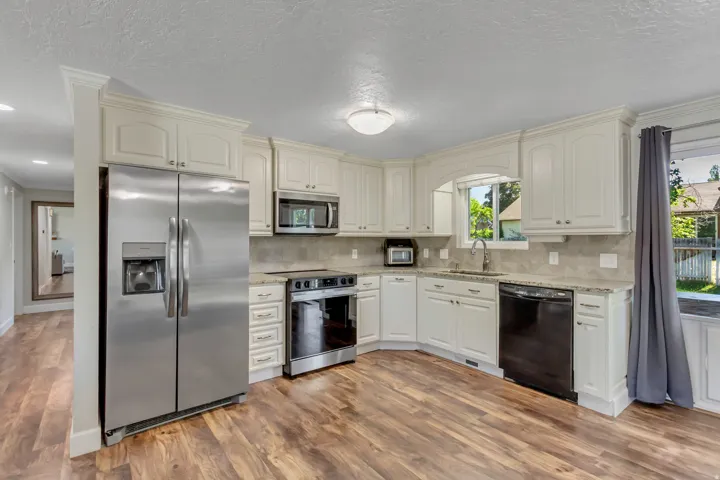 Spacious kitchen featuring wood-finish flooring, white cabinetry with crown molding, stainless steel appliances, granite countertops, and a tiled backsplash