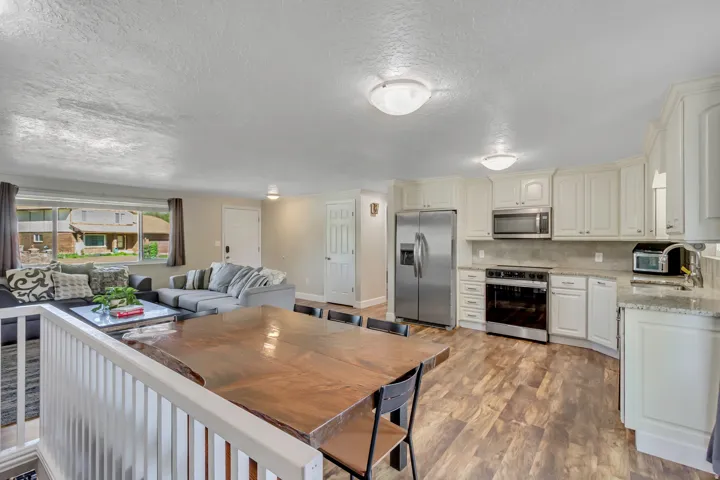 Open-concept living space featuring a kitchen with light-toned cabinetry, stainless steel appliances, and granite-style countertops