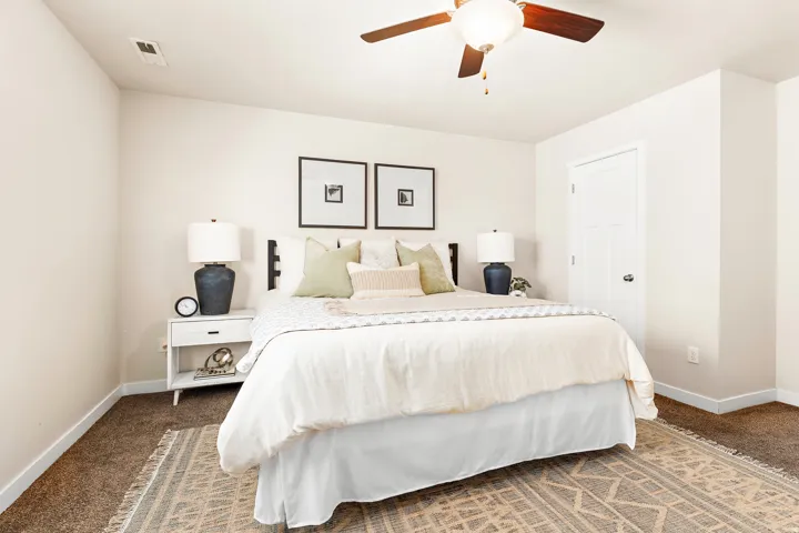 Spacious bedroom featuring neutral wall tones, plush carpeting, a ceiling fan with integrated lighting, and a paneled white door
