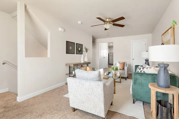 Open concept living area featuring textured carpeting, a ceiling fan with light, and a staircase with a handrail