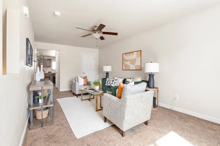 Spacious living area featuring neutral-toned walls, brown carpeting, and a ceiling fan with integrated lighting