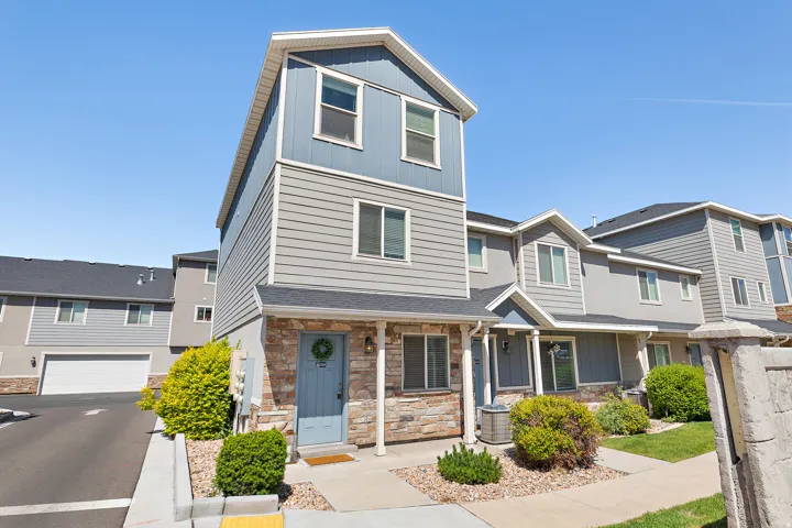 Contemporary exterior featuring multi-level siding in varied tones, a covered entryway with stone accents, a light blue front door, and a manicured landscape with shrubs and gravel