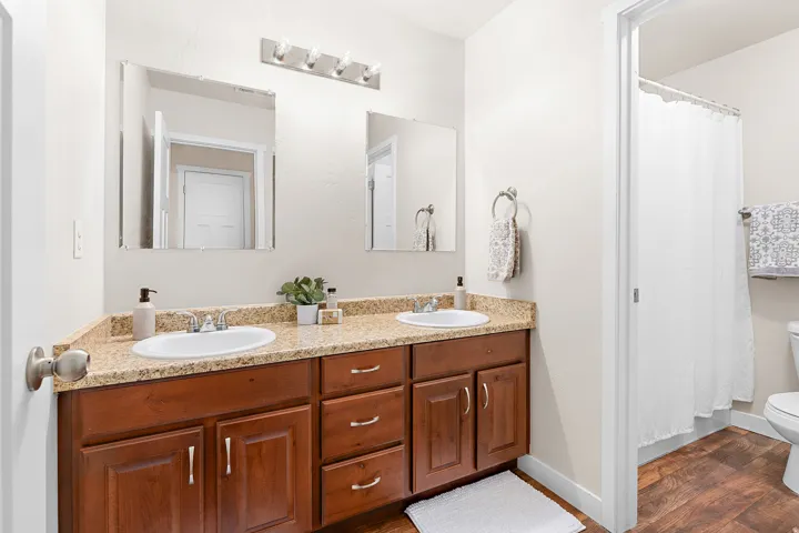 Double vanity featuring two undermount sinks, granite-look countertops, and rich wood-finish cabinetry with brushed nickel hardware