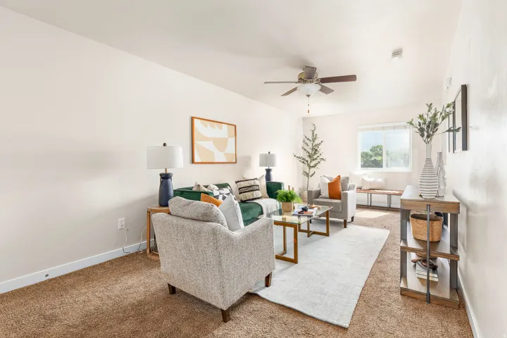 Spacious living area featuring neutral-toned walls, plush carpet, and a ceiling fan with integrated lighting