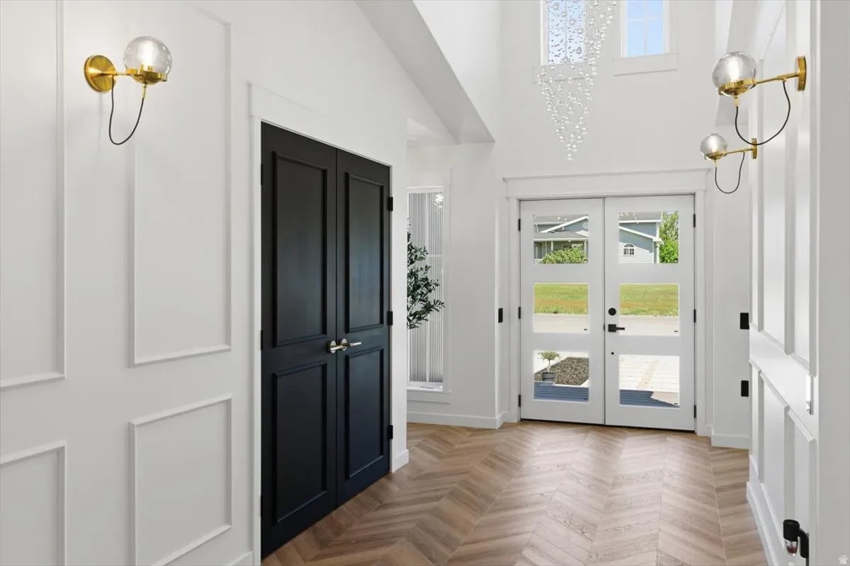 Double-height entry featuring herringbone wood-finish flooring, white paneled walls, and transom windows